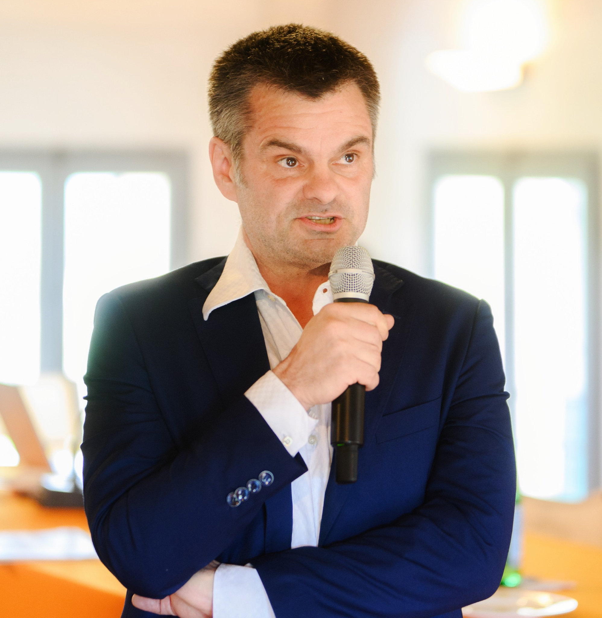 Man speaking into a microphone, wearing suit.